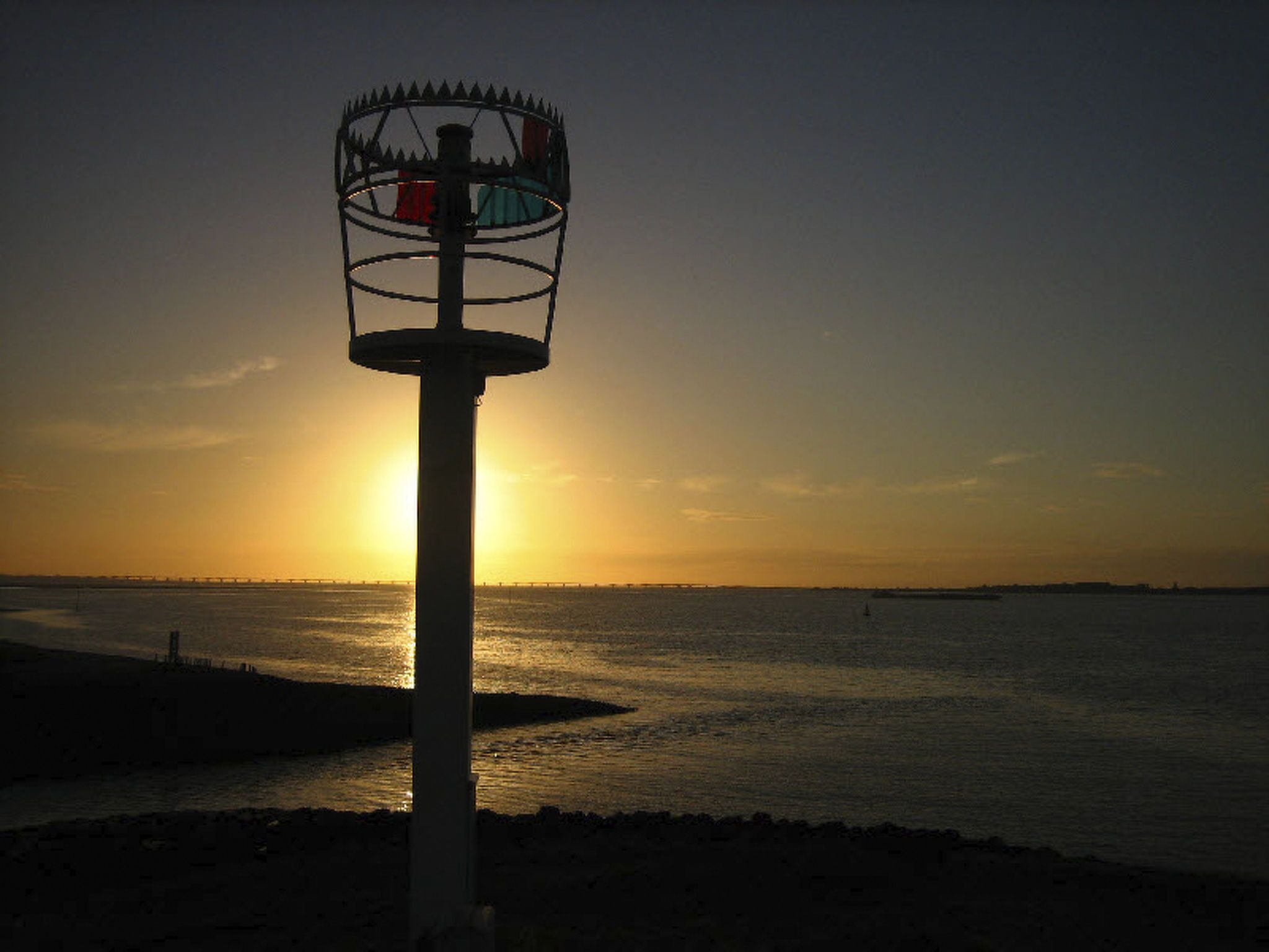 A lighthouse by the sea during sunset.