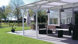 Un patio couvert, aménagé avec du mobilier d’extérieur, un mur en briques et offrant une vue sur la cour environnante.