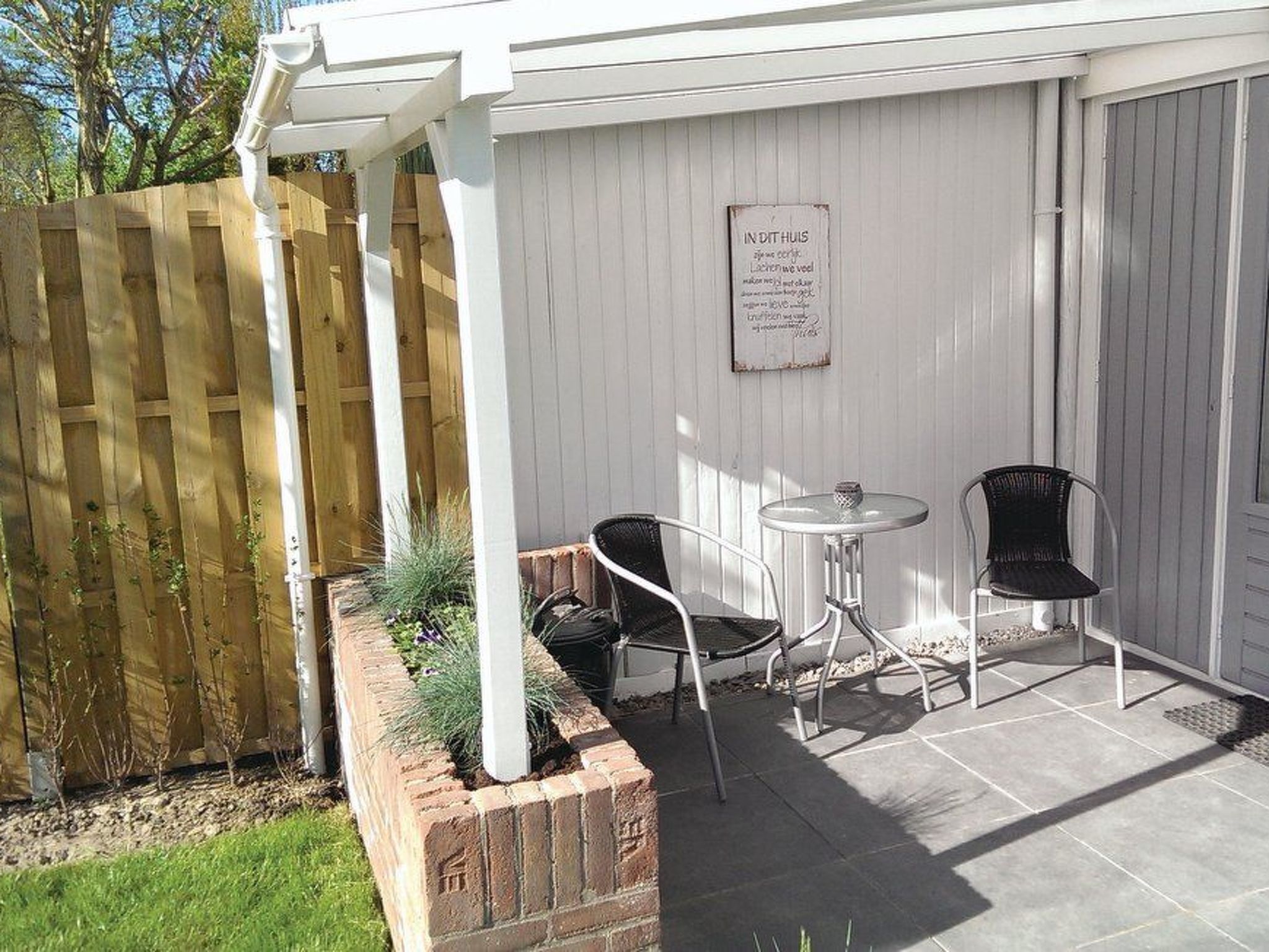 Eine Terrasse mit zwei Stühlen, einem kleinen Tisch, einem Holzzaun und einem Schild an der Wand.