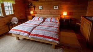Un dormitorio de cabaña de madera acogedor, con una cama grande, dos lámparas de noche, un aparador de madera y una ventana con cortina de encaje.