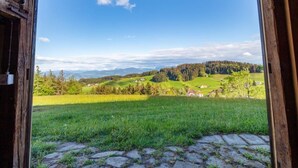 Una puerta de madera abierta a una vista panorámica de un paisaje verde con campos, árboles y montañas distantes.