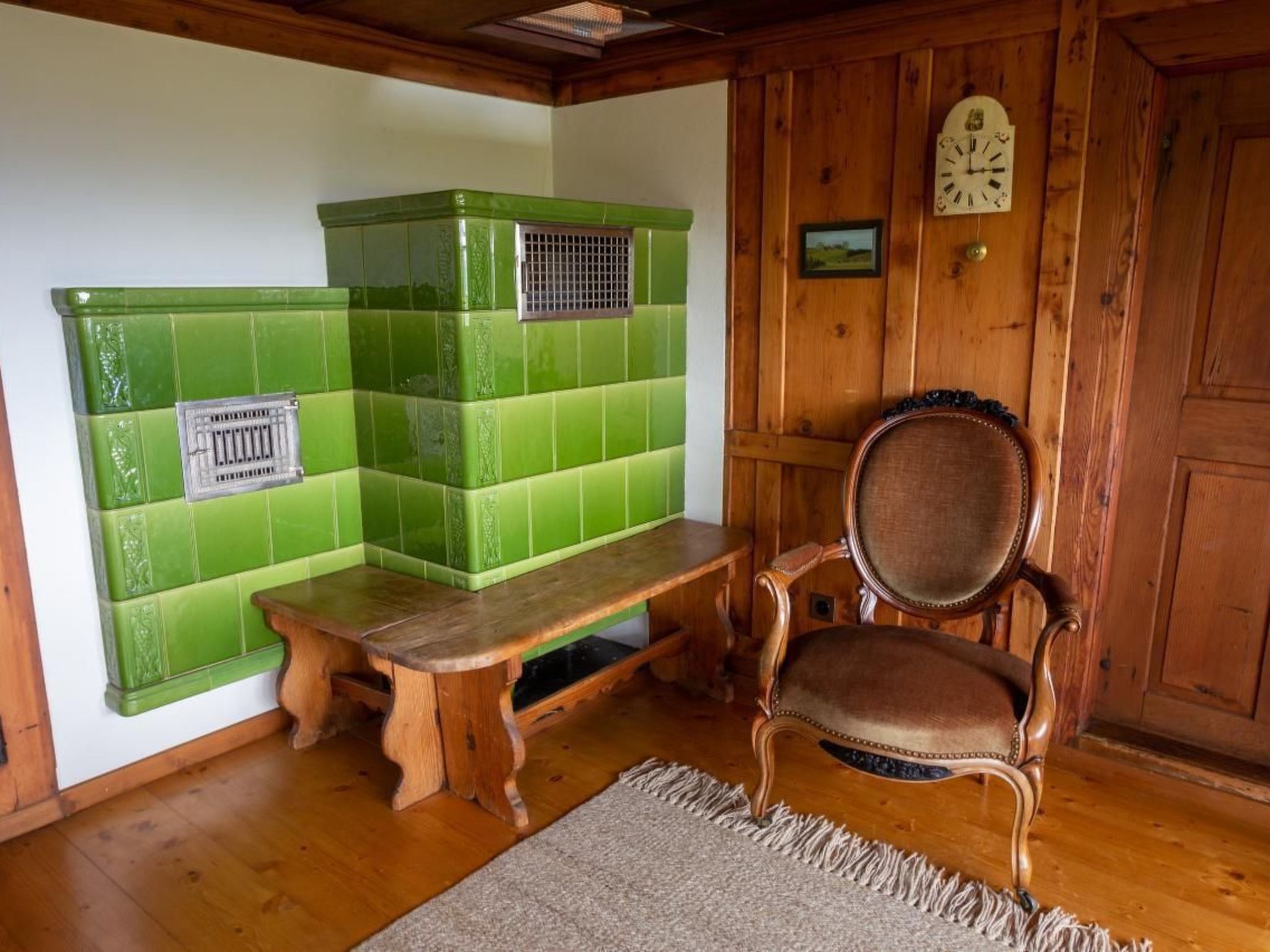A room with a wooden bench, a green tiled wall, a wooden door, and a wall clock.