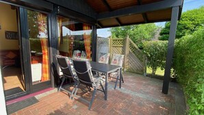 A covered patio with a table and chairs, a wooden fence, and a view of a garden. - Vacation home L 2 by Interhome (Burhave)