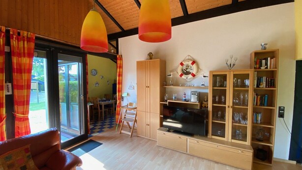 A living room with a wooden ceiling, a television, a bookshelf, and a dining area with a checkered floor. - Vacation home L 2 by Interhome (Burhave)