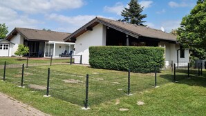 A two-story building with a tiled roof, a covered patio with chairs, and a well-maintained lawn. - Vacation home L 2 by Interhome (Burhave)