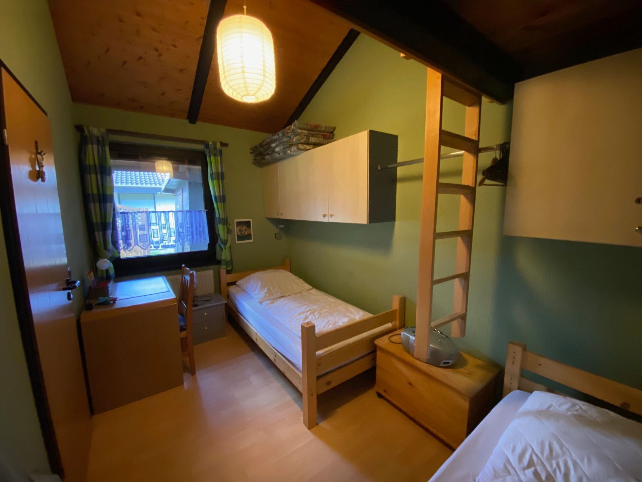 Una habitación pequeña y acogedora con una cama litera, un escritorio con silla, una ventana con cortinas y una escalera de madera.