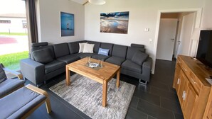 A modern living room with a sectional sofa, a wooden coffee table, and a large window with curtains. - N4 Haus in Nordseenähe mit Terrasse und Garten by Interhome (Burhave)