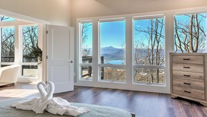 A spacious bedroom with large windows, a ceiling fan, and a wooden dresser. - Skyline Ridge | Modern New Build with Long Range Blue Ridge Mountain Views in Arden (Arden)