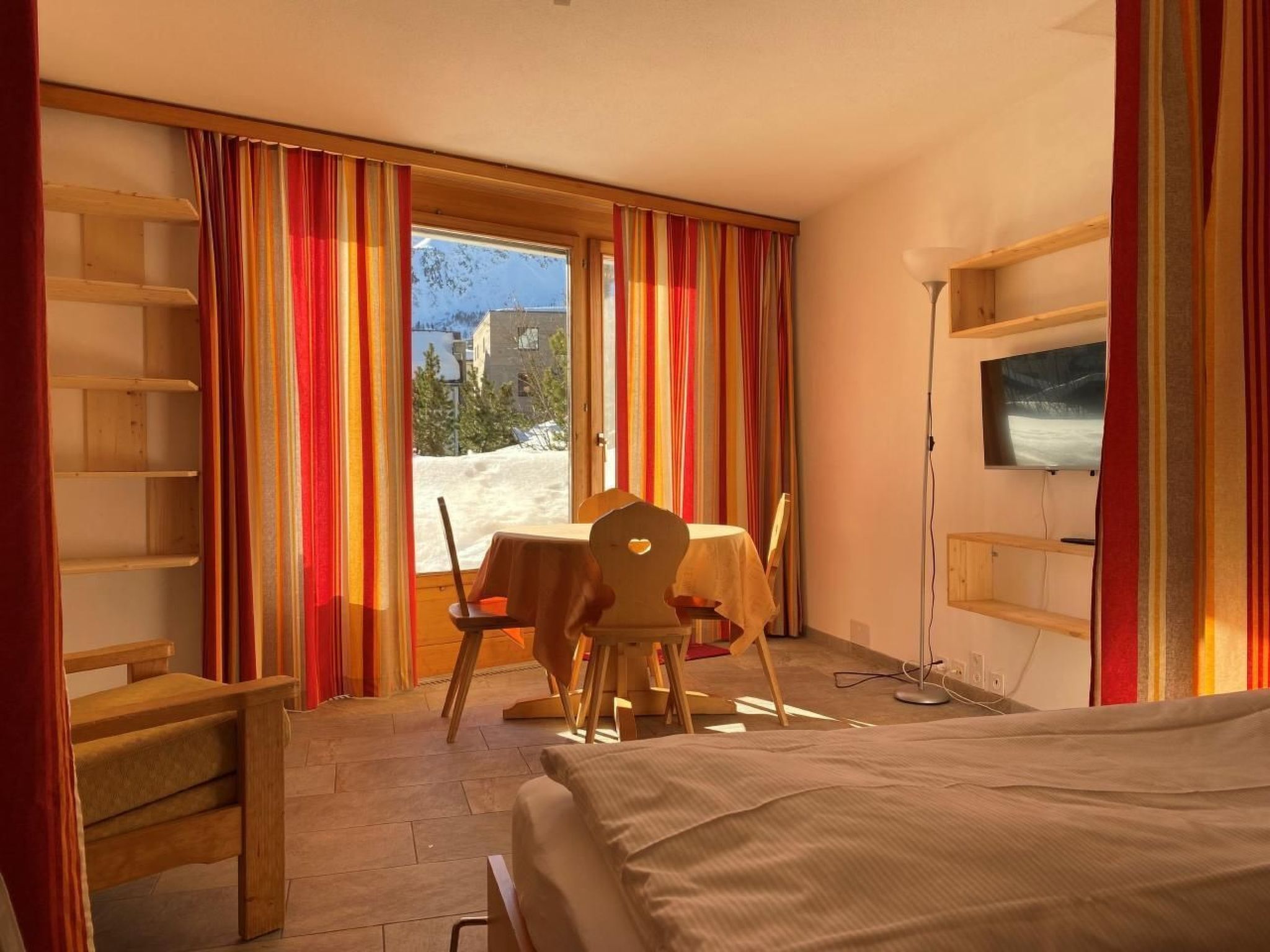 A hotel room with a bed, a desk, a chair, a table, and a TV.