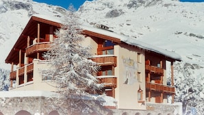 A multi-story wooden building with balconies, surrounded by snow-covered mountains. - Apparthotel Pöstli Nr. 106 by Interhome (Maloja)