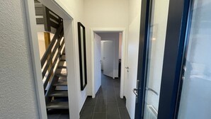 Ein Flur mit Treppe, einer Tür mit Fensterteil und einem Fliesenboden.