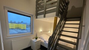 Ein Schlafzimmer mit Bett, Nachttisch, Fenster mit Blick auf eine verschneite Landschaft und einer Treppe.