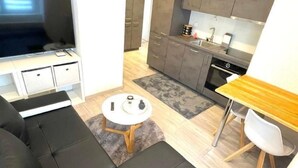 A modern living room with a black leather sofa, a flat-screen TV, and a dining area with a wooden table and white chairs. - Appartement mit privatem Parkplatz by Interhome (Unterterzen)