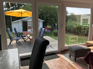 Una habitación con una puerta corrediza de vidrio que da a un patio con mobiliario exterior y un paraguas amarillo.