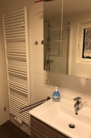 Ein Badezimmer mit einem weißen Waschbecken, einer Glasdusche, einem weißen Handtuchhalter und einer Flasche Pure Flussigseife Seife.