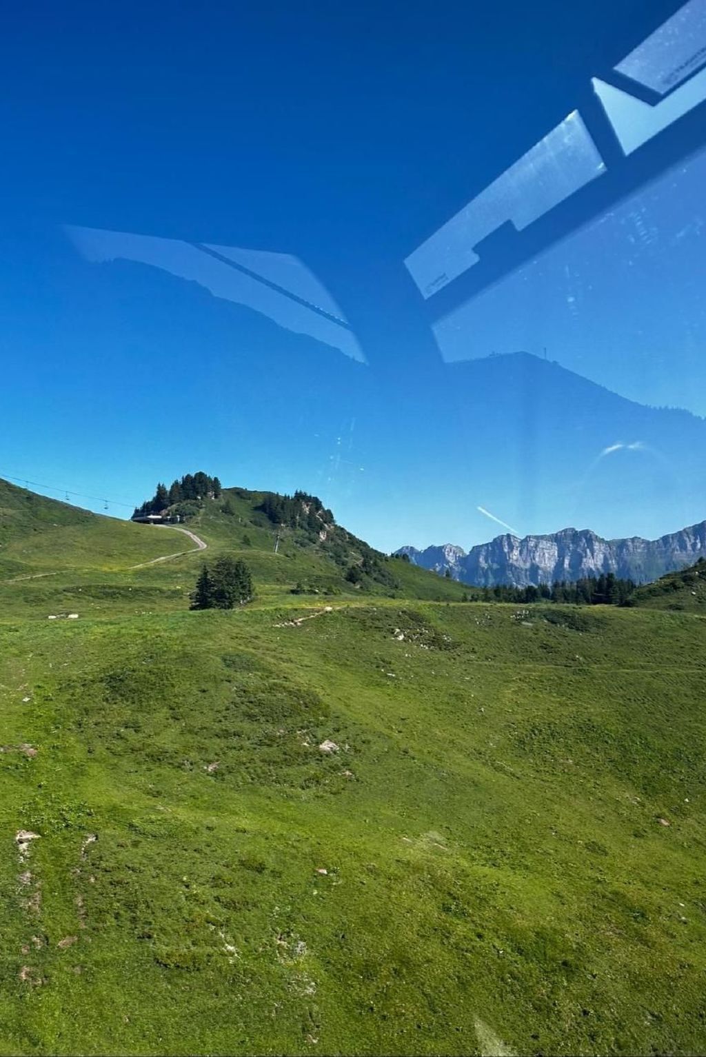 Et panorama over et bjergrigt landskab med klar himmel, en snoet sti og en lille bakke med træer.