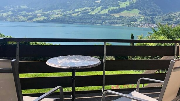 Un balcon avec une table et des chaises donnant sur un lac et des montagnes.