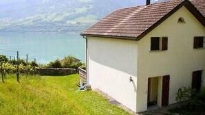 Une maison de plain-pied avec un toit en pente, un petit porche et une vue sur un lac et des montagnes en arrière-plan.