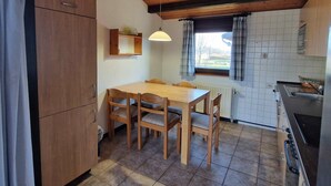 Eine kompakte Küche mit Holzausstattung, einem Esstisch mit Stühlen, einer Pendelleuchte und Blick durch ein fensterbehangenes Fenster.