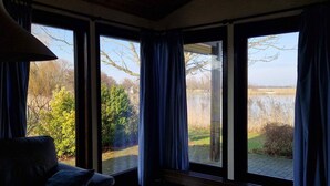 Ein Zimmer mit großen Fenstern, einer Holzbalkendecke und einem dunkelbraunen Sofa.