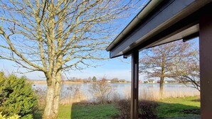 Ein See mit einem Baum im Vordergrund und einem Gebäude mit überdachter Terrasse.