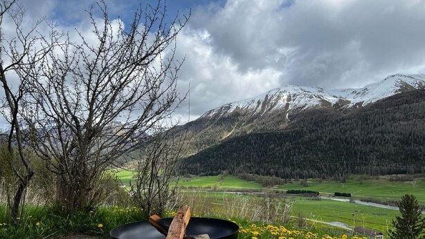 Una parrilla exterior negra con leña, sobre una superficie de concreto con vistas a un paisaje montañoso y un río.