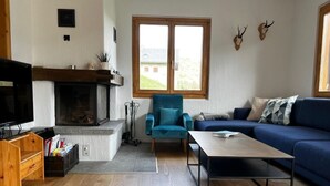 Una sala de estar con chimenea, un sillón azul, un sofá y una mesita de centro.