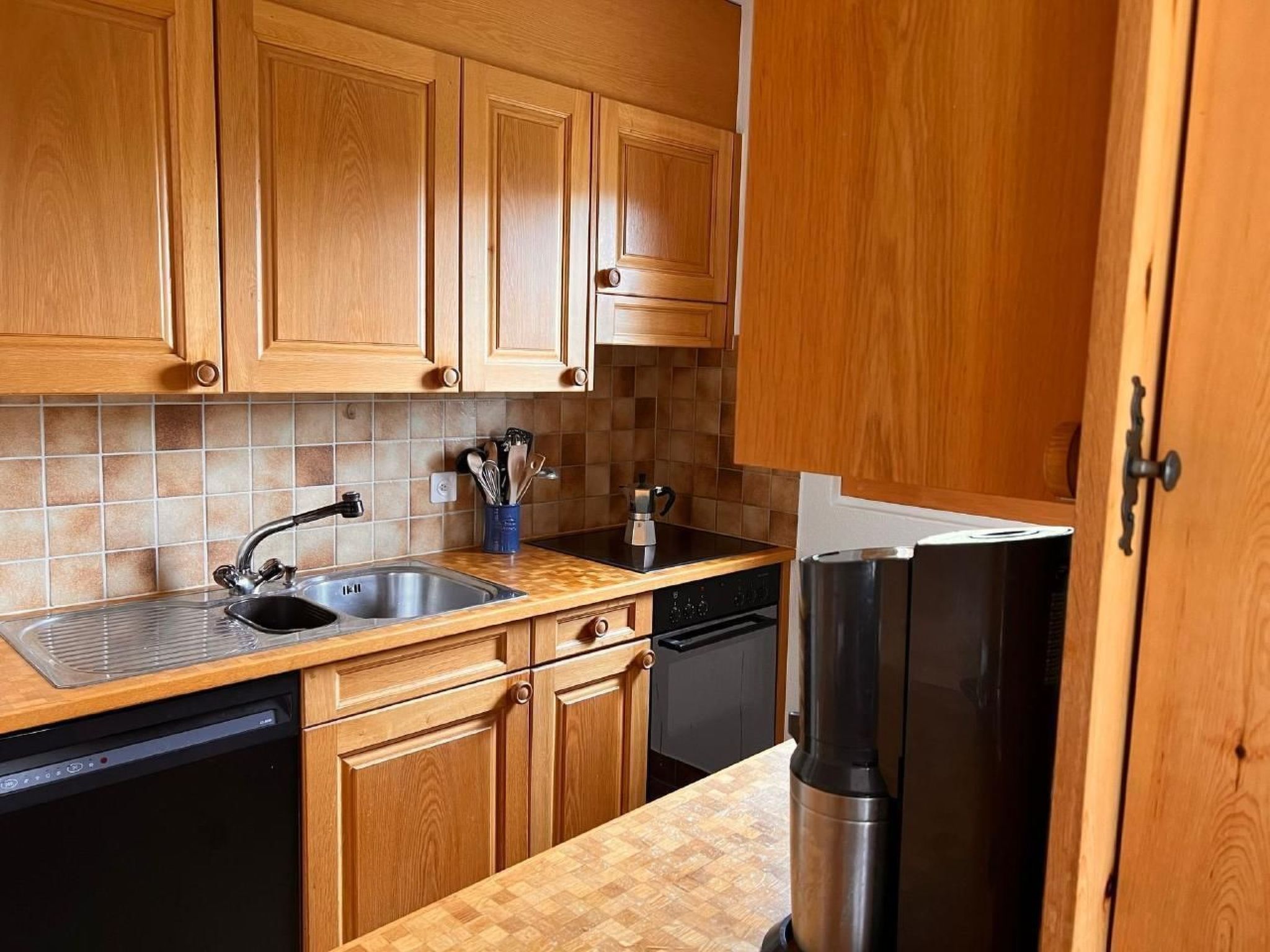 Eine Küche mit Holzschränken, einem Edelstahlkühlschrank, einer Spülmaschine und einer gefliesten Spritzschutzwand.
