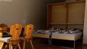 Una habitación moderna con una mesa de comedor y sillas, una cama con cabecera de madera, y una lámpara colgante.