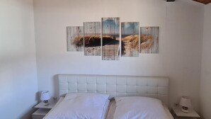 Makuuhuoneessa on suuri sänky, valkoiset vuodevaatteet, puinen katto ja seinälle ripustettu taideteos, jossa on kuvattu rantamaisema.