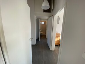 Ein schmaler Korridor mit einer Tür links, einem Holzschrank rechts und einem Badezimmer im Hintergrund.