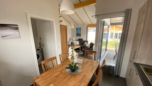 A dining area with a wooden table and chairs, a vase of white flowers, and pendant lighting. - N11 Ferienhaus mit Garten in Eckwarderhörne by Interhome (Burhave)