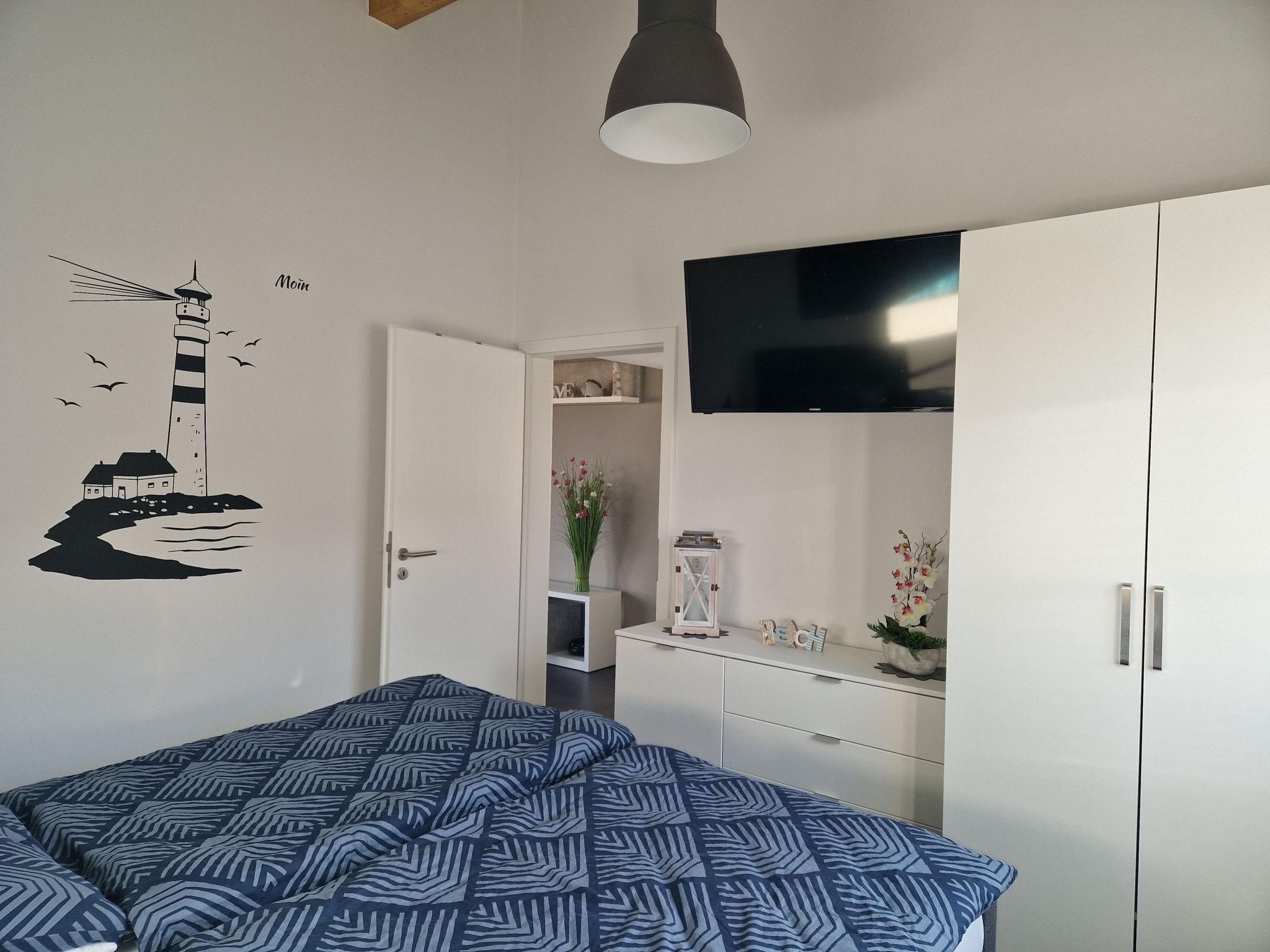 A bedroom with a bed, a TV, a wardrobe, and a wall decoration of a lighthouse.