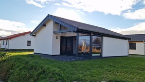 Ein modernes, zweistöckiges Haus mit geneigtem Dach, großen Glasfenstern und einer überdachten Terrasse.