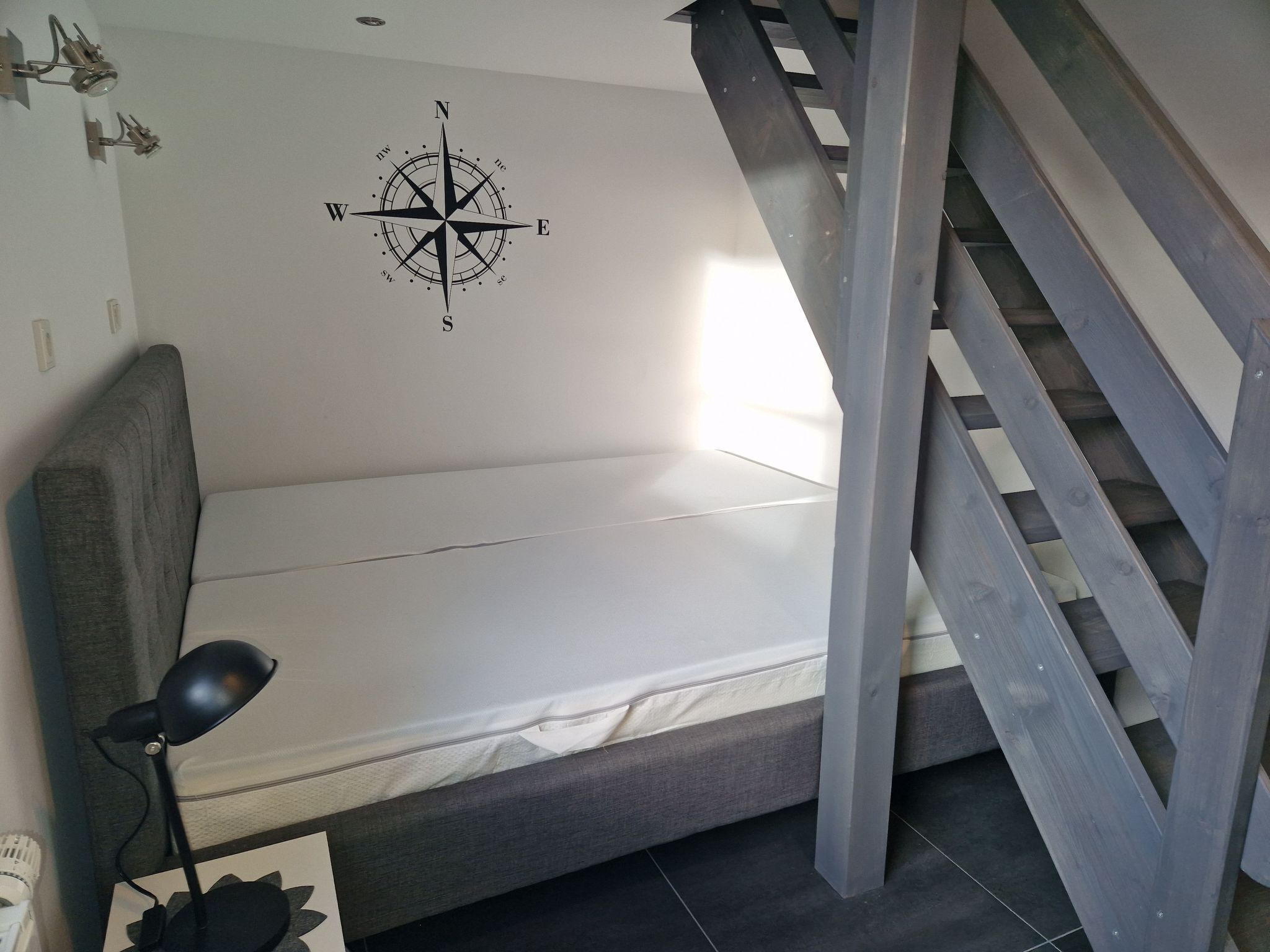 Ein Schlafzimmer mit einem Bett, einer Schreibtischlampe, einer Kompass-Wanddekoration und einer Treppe.