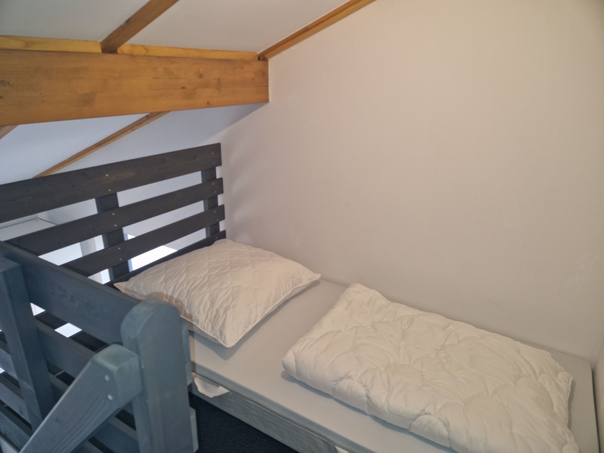 A small, single-bed room with a wooden headboard and a simple white mattress.