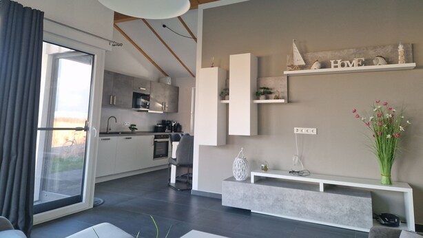 Eine moderne Küche mit integrierten Geräten, ein Essbereich mit einer Couch und einer Pendelleuchte sowie ein Wohnbereich mit einer Konsolentisch und Dekorationselementen.