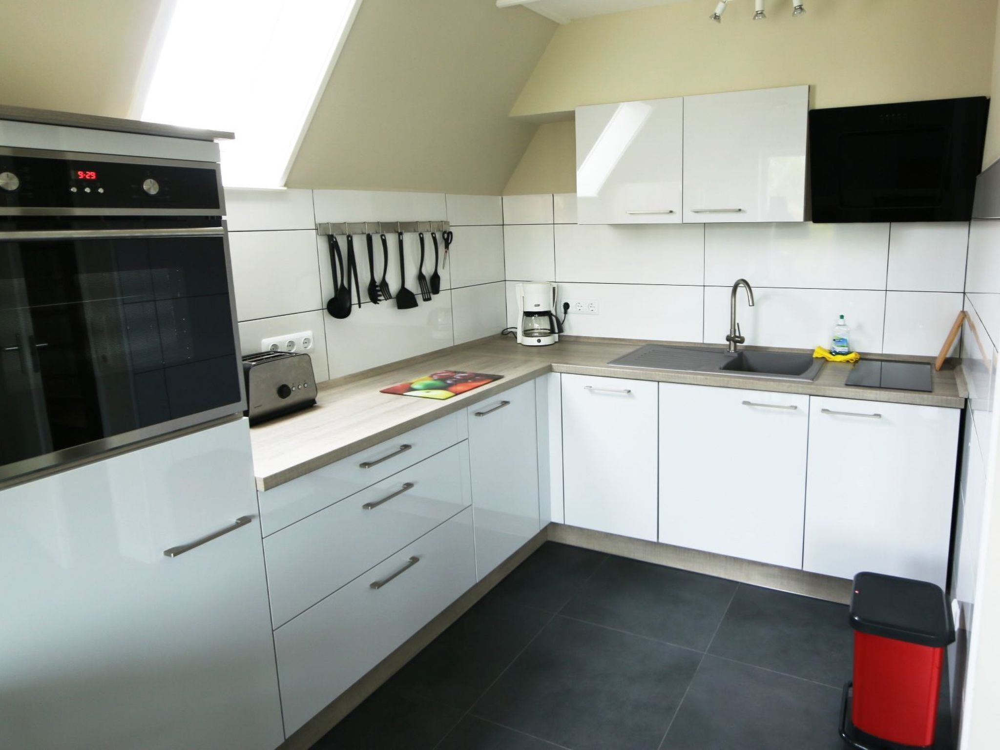 Een moderne keuken met witte kastjes, een zwarte oven, een koffiezetapparaat en een spoelbak.