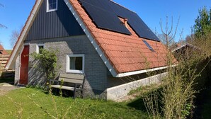 Una casa con tetto spiovente, una piccola finestra e una panchina nel cortile.