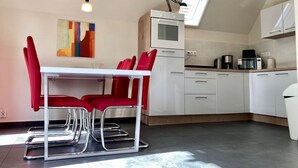 Una cucina moderna con mobili bianchi, un tavolo da pranzo con sedie rosse e un lucernario sopra.