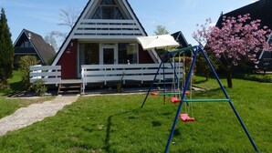 Una casa con techo triangular, un porche con cerca blanca y un columpio en el jardín.