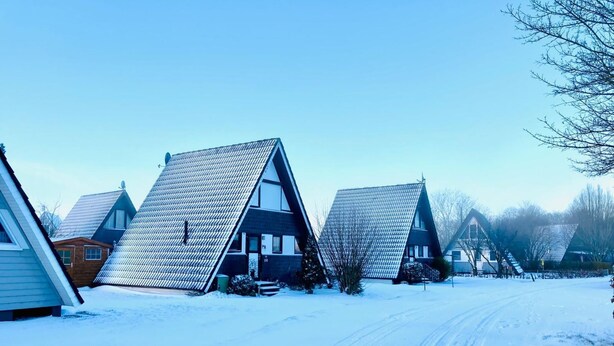 Una hilera de casas cubiertas de nieve con techos empinados, cielo despejado y una carretera nevada.