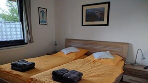 A double bed with two pillows, a bedside table with a lamp, and a window with curtains. - K3 Ferienhaus Eul by Interhome (Burhave)