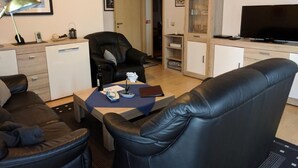 A modern living room with a leather sofa, a dining area with a table, a black leather chair, a TV, and a cabinet with glass doors. - K3 Ferienhaus Eul by Interhome (Burhave)