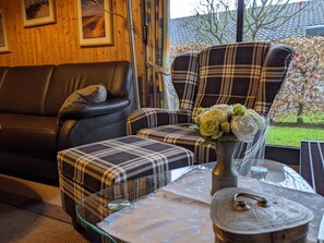 A cozy living room with a leather sofa, plaid armchairs, a glass coffee table with a decorative lid, and a vase of flowers. - Vacation home Eul F5 by Interhome (Burhave)