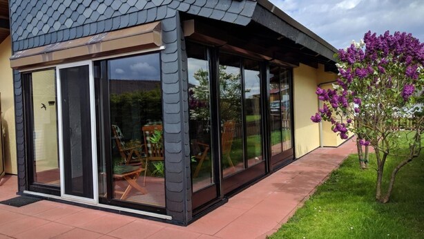 Una casa con patio coperto, porte scorrevoli in vetro e un giardino fiorito di fiori viola.