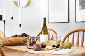 Et træbord med vin, glas, ost, frugt og nødder.
