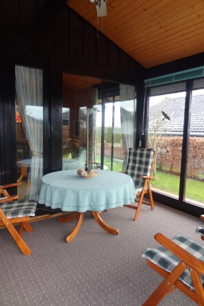 Una habitación con una mesa redonda, dos sillas, una ventana con cortinas y vistas a un jardín.