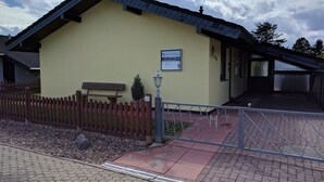 A building with a yellow facade, a wooden fence, a bench, and a sign. - Eul Ferienhaus F5 by Interhome (Burhave)