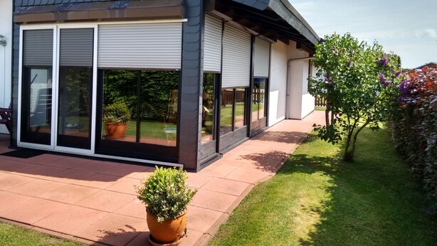 A modern house with a covered patio, large sliding glass doors, and a potted plant in the foreground. - Eul Ferienhaus F5 by Interhome (Burhave)